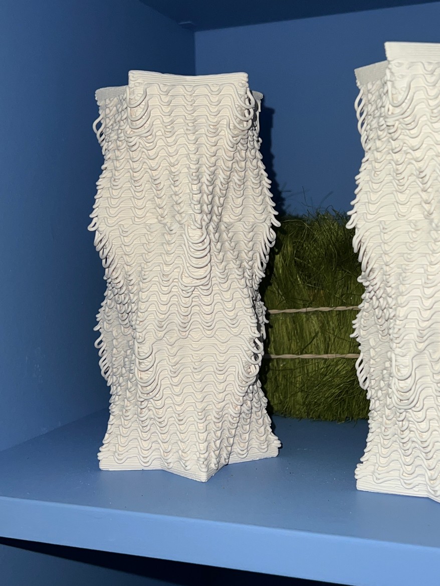 Two white 3D-printed vessels with wavy layered walls on a blue shelf